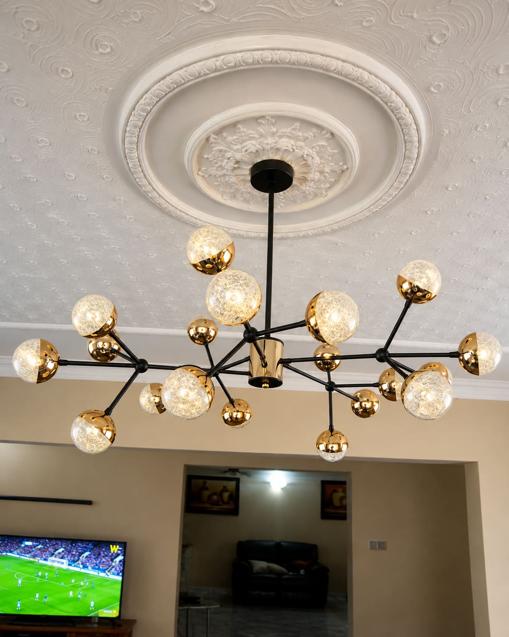Black and gold multi-globe chandelier hung from an ornate plaster ceiling rose in a lounge