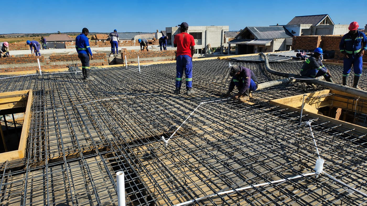 Construction team pouring concrete over a reinforced slab with electrical conduit boxes already positioned